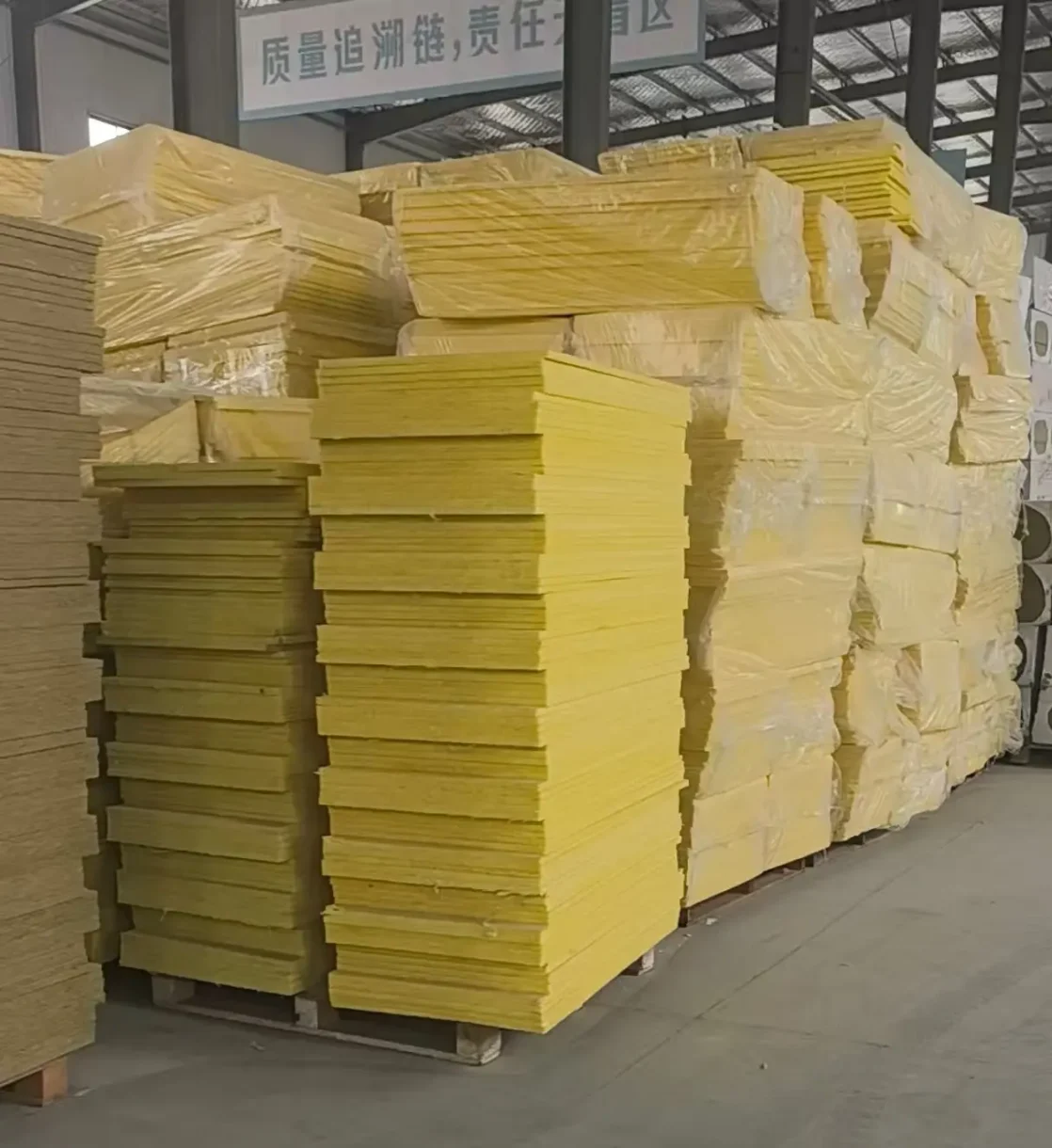 Stacks of yellow fiberglass acoustic panel core boards in a manufacturing factory warehouse