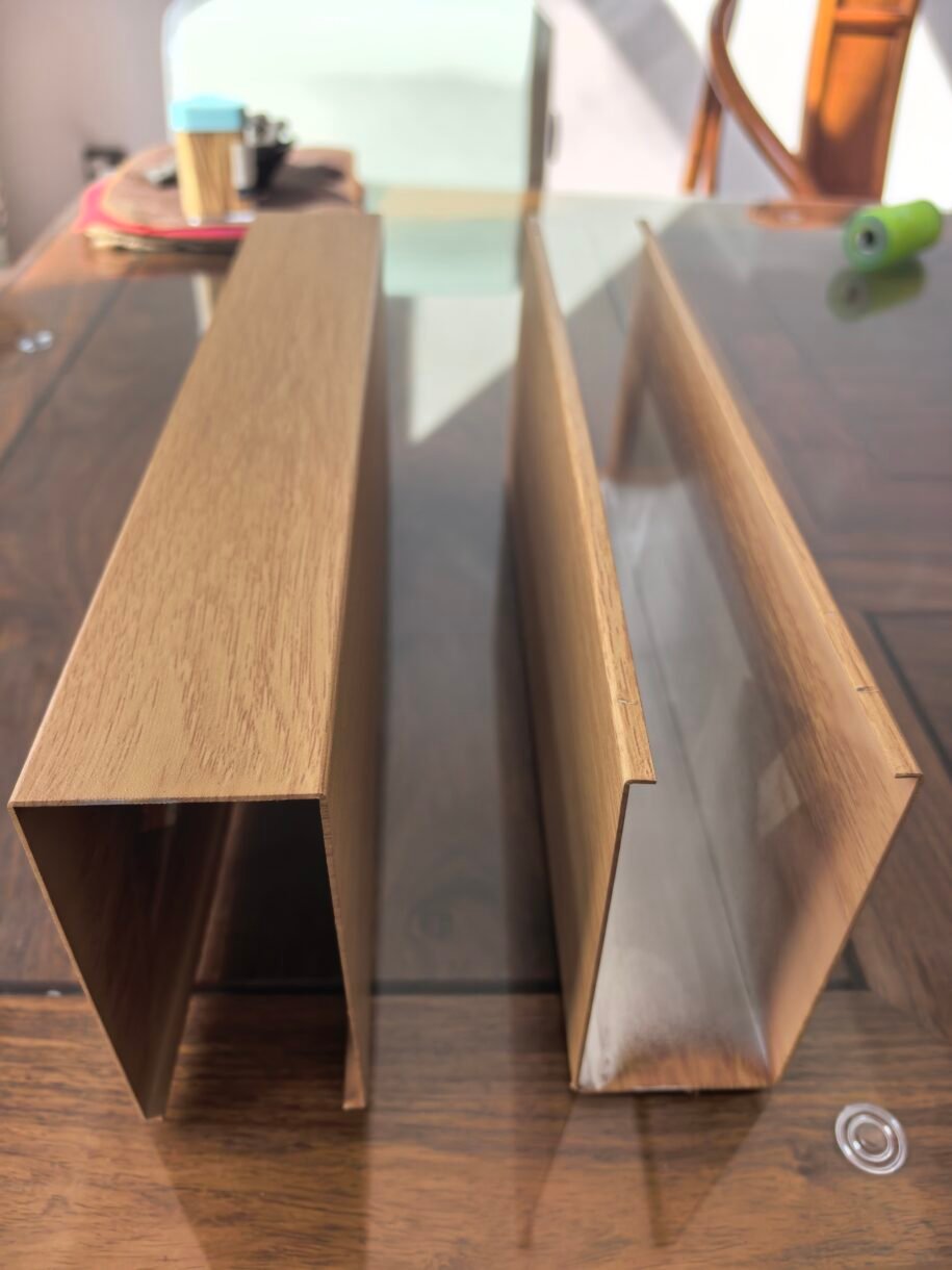 U-shaped aluminum baffle samples showing a wood-grain finish and exposed metal profile interiors