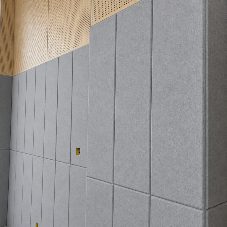 Grey fabric-wrapped fiberglass acoustic panels being installed on an interior wall surface for commercial noise reduction.