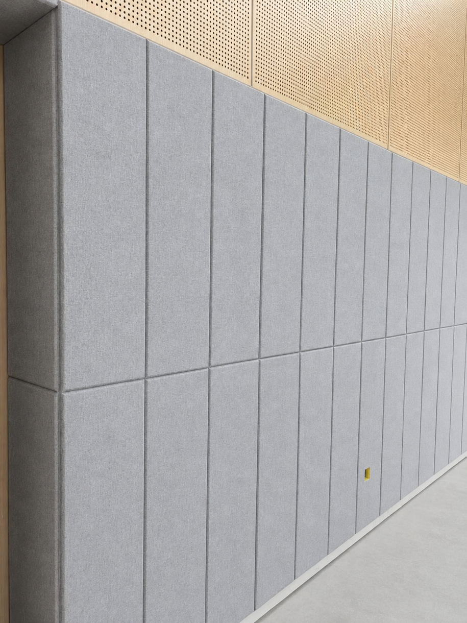 A finished interior wall featuring vertically aligned, grey fabric-wrapped fiberglass acoustic panels for commercial soundproofing.