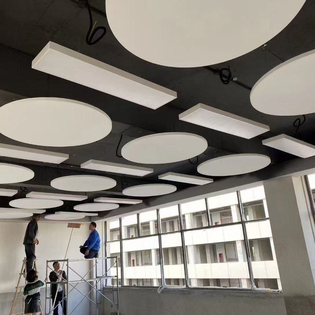 Suspended white fiberglass acoustic ceiling clouds and baffles installed in a commercial high-bay building.